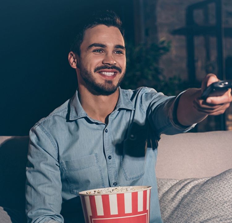 Person lächelt und hält eine Fernbedienung Richtung Fernseher.